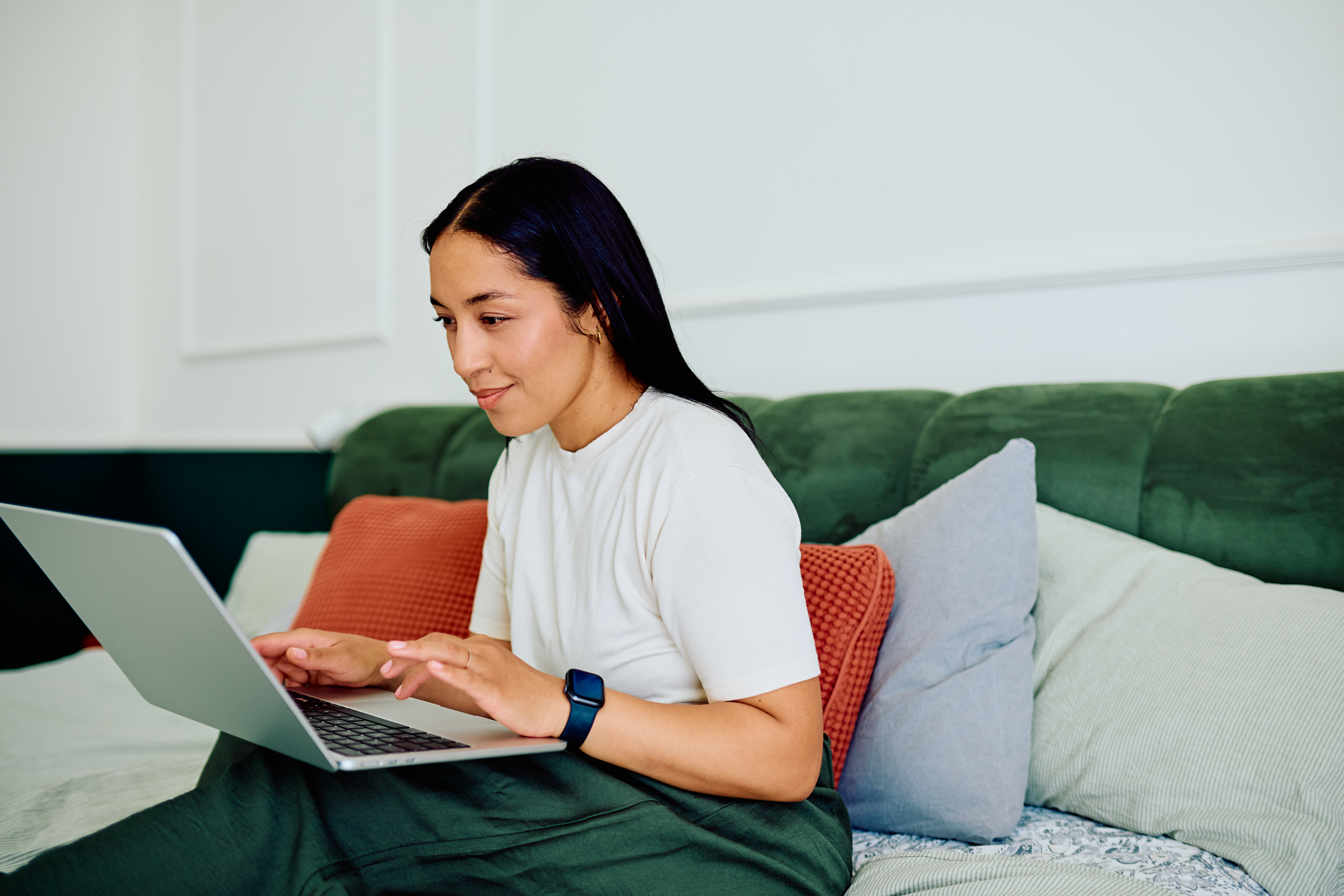 Happy woman remotely working from home, typing on a laptop computer while sitting comfortably in bed